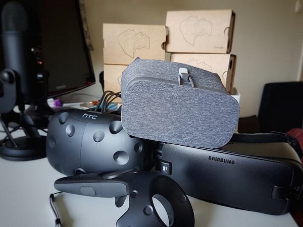 Фотография очков виртуальной реальности HTC Vive с контроллером положения, а также гарнитур Samsung Gear VR, Google Daydream и Google Cardboards на заднем плане